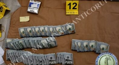 Evidence board showing several bundles of U.S. hundred-dollar bills laid out in rows, with a 'Smoking kills' cigarette pack and a yellow 12 marker nearby.