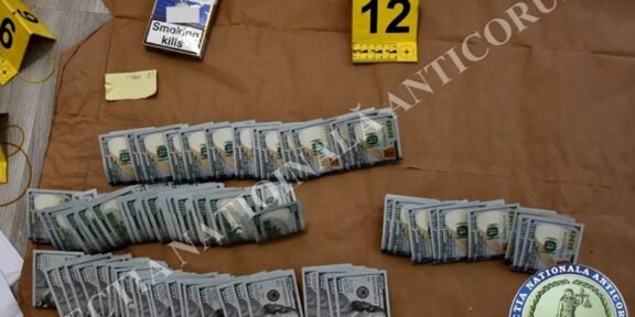 Evidence board showing several bundles of U.S. hundred-dollar bills laid out in rows, with a 'Smoking kills' cigarette pack and a yellow 12 marker nearby.