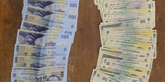 Two stacks of Romanian banknotes on a wooden table: blue 100-leu notes on the left and brownish 50-leu notes on the right.