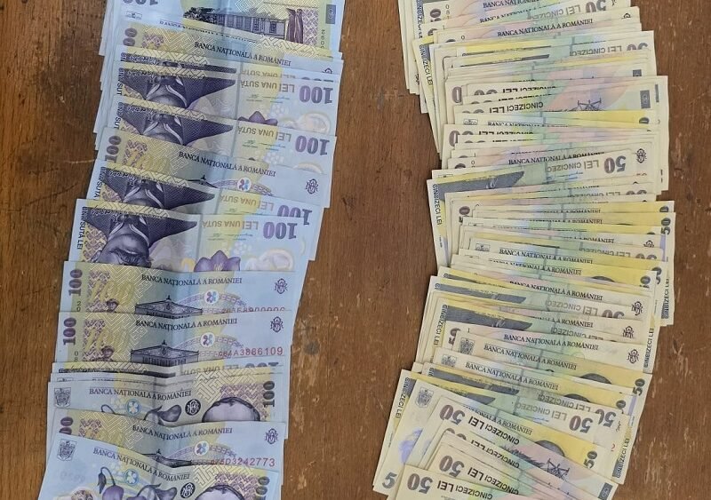 Two stacks of Romanian banknotes on a wooden table: blue 100-leu notes on the left and brownish 50-leu notes on the right.