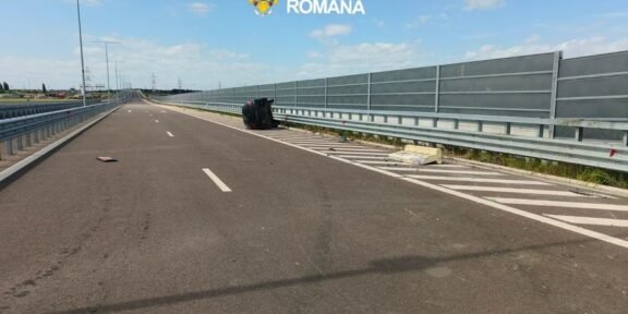 Wide highway scene with an overturned dark car on the right shoulder near the barrier; police logo reads 'Poliția Română'.
