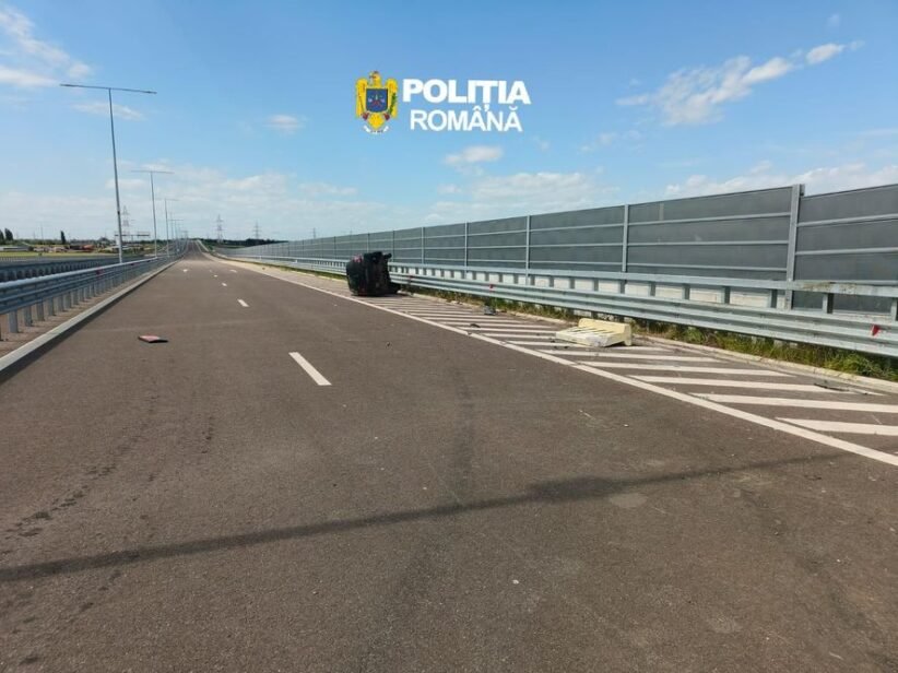 Wide highway scene with an overturned dark car on the right shoulder near the barrier; police logo reads 'Poliția Română'.