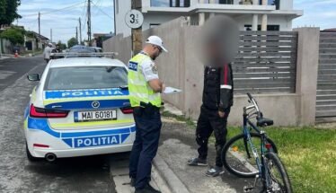 Policeman in a reflective vest writes on a clipboard beside a police car on a residential street.