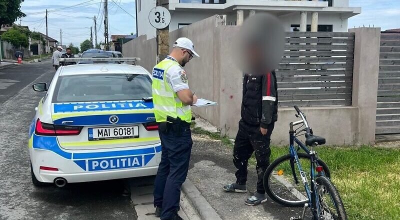Policeman in a reflective vest writes on a clipboard beside a police car on a residential street.