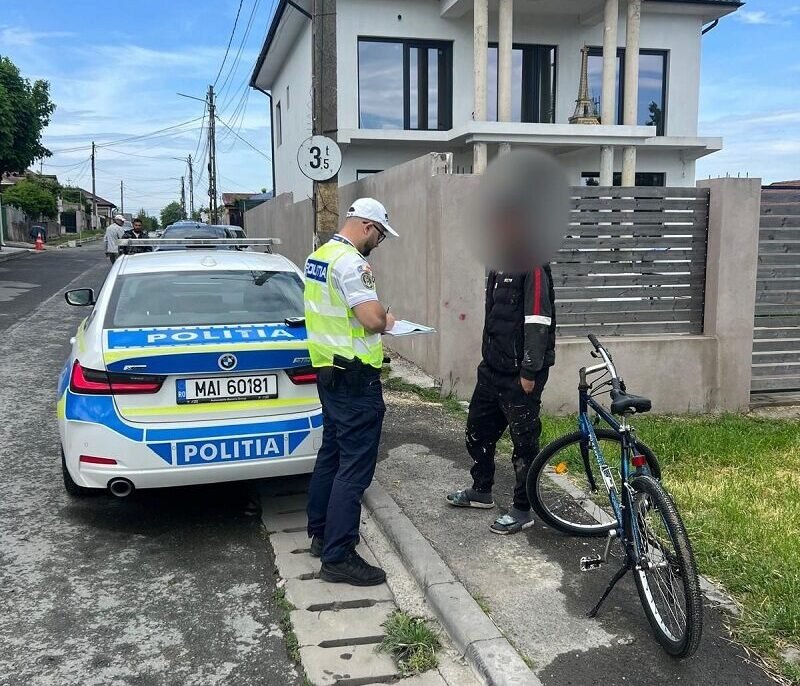 Policeman in a reflective vest writes on a clipboard beside a police car on a residential street.