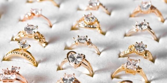 Assortment of gold engagement rings with diamonds arranged on a white display surface.