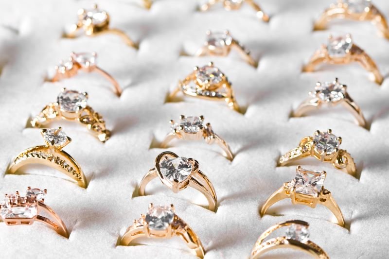Assortment of gold engagement rings with diamonds arranged on a white display surface.
