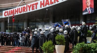 Riot police in helmets and shields facing a crowd outside a building with a large red sign that reads Cumhuriyet Halk.
