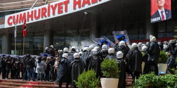 Riot police in helmets and shields facing a crowd outside a building with a large red sign that reads Cumhuriyet Halk.