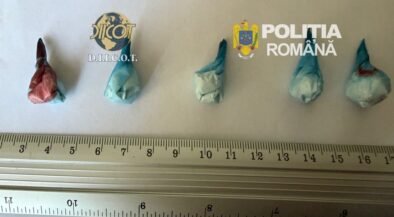 Five small wrapped parcels laid out on a ruler for scale; logos of DIICOT and Romanian Police in the background, suggesting a drug seizure display.