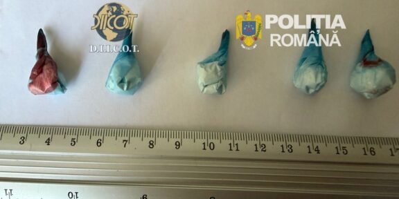 Five small wrapped parcels laid out on a ruler for scale; logos of DIICOT and Romanian Police in the background, suggesting a drug seizure display.