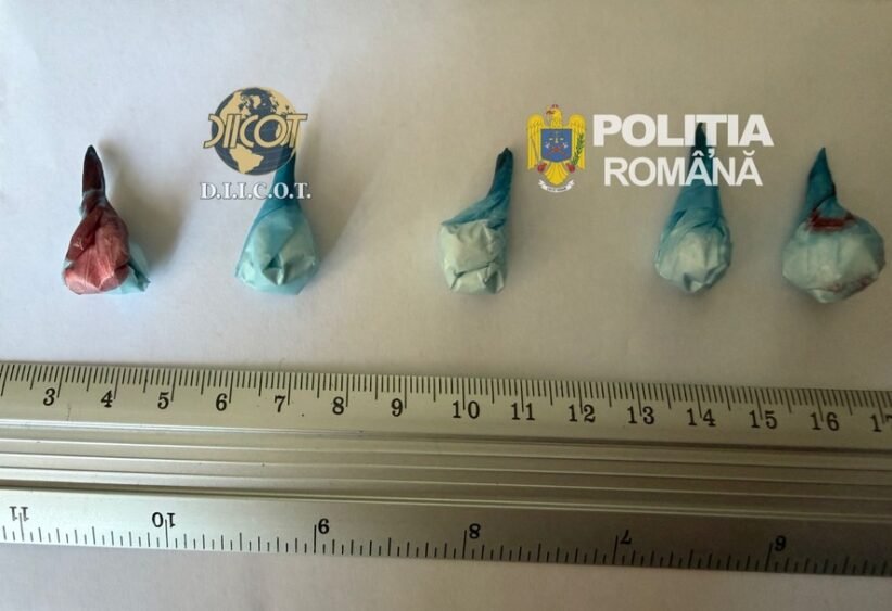 Five small wrapped parcels laid out on a ruler for scale; logos of DIICOT and Romanian Police in the background, suggesting a drug seizure display.