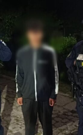 Two gendarmes in tactical gear flank a blurred civilian on a cobblestone path at night.