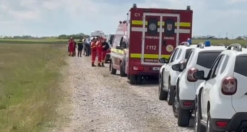 Emergency scene on a rural gravel road: a red ambulance, white parked cars, and firefighters in orange uniforms
