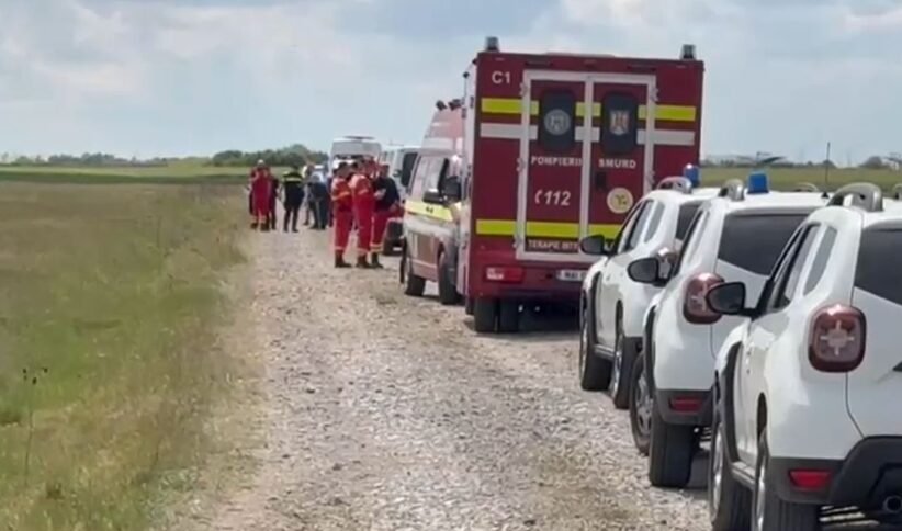 Emergency scene on a rural gravel road: a red ambulance, white parked cars, and firefighters in orange uniforms