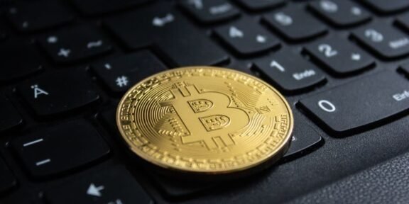Gold Bitcoin coin resting on a black computer keyboard in close-up.