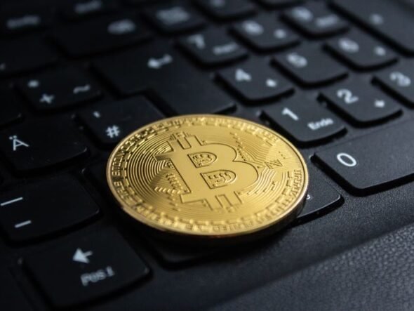 Gold Bitcoin coin resting on a black computer keyboard in close-up.