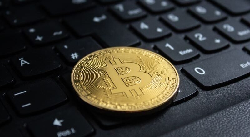Gold Bitcoin coin resting on a black computer keyboard in close-up.