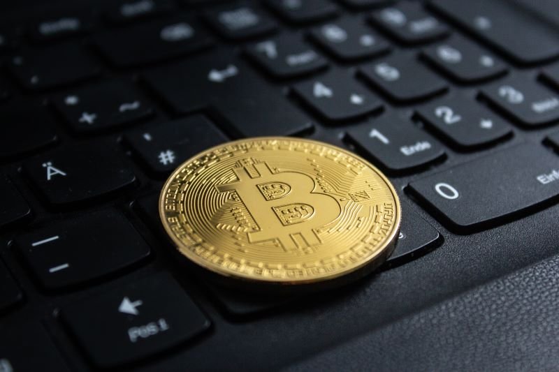 Gold Bitcoin coin resting on a black computer keyboard in close-up.