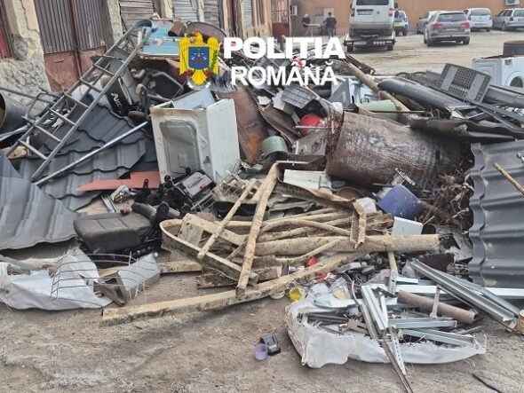 Pile of scrap metal, wood, and debris scattered on a street with a police logo overlaid and parked cars in the background, indicating a cleanup scene.