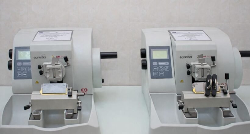 Two compact gray laboratory instruments with control panels sit side by side on a lab bench, each with a sample clamp and cutting area.