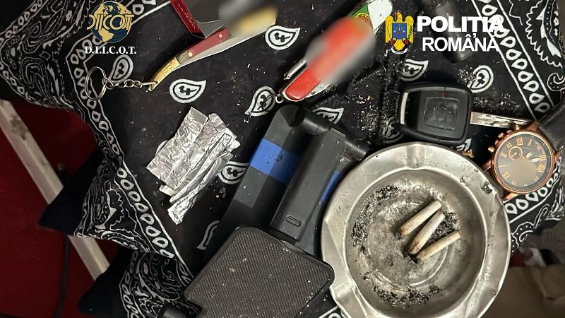 Police evidence photo: cigarette butts in an ashtray, foil packets, a lighter, and other paraphernalia on a patterned cloth with Romanian police logos visible.