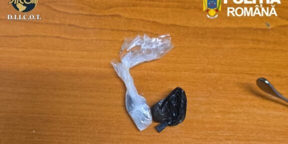 Two small plastic bags, one transparent and one black, lie on a wooden desk with police logos (Romania) in the corners, suggesting seized evidence.