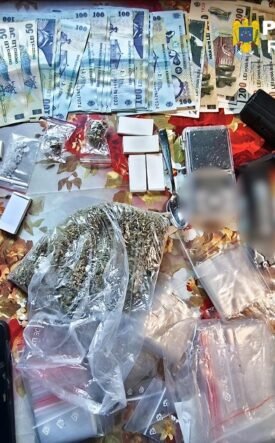 Romanian police display confiscated items on a table: euro banknotes, small bags of drugs, a handgun, and several smartphones.