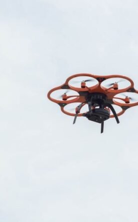 Orange hexacopter drone with six propeller arms hovering in a pale blue sky