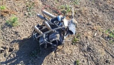 Mess of tangled wires and metal tubes on dry, rocky ground outdoors.