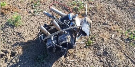 Mess of tangled wires and metal tubes on dry, rocky ground outdoors.