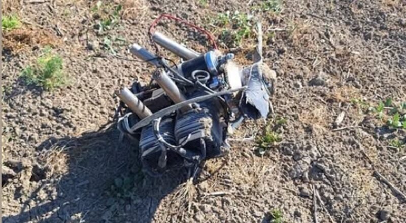 Mess of tangled wires and metal tubes on dry, rocky ground outdoors.