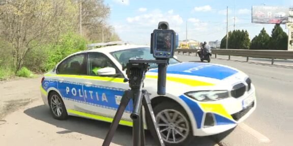 Romanian police car on a road with a speed camera mounted on a tripod in the foreground.