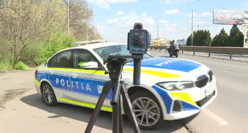 Romanian police car on a road with a speed camera mounted on a tripod in the foreground.