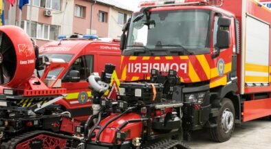 Red fire trucks with yellow chevrons parked in a lot, with a red tracked rescue robot in the foreground.