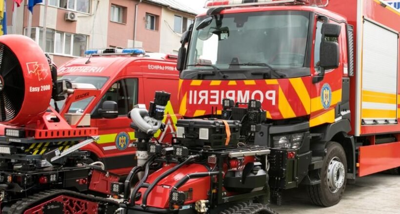 Red fire trucks with yellow chevrons parked in a lot, with a red tracked rescue robot in the foreground.