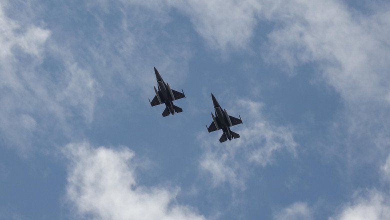 Two fighter jets in formation flying through a partly cloudy blue sky.
