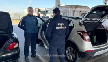 Border police officer in a dark uniform talks to a man at a car with the trunk open at a checkpoint. Frontière police patch visible on the jacket (text: POLIŢIA DE FRONTIERĂ).
