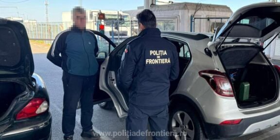 Border police officer in a dark uniform talks to a man at a car with the trunk open at a checkpoint. Frontière police patch visible on the jacket (text: POLIŢIA DE FRONTIERĂ).
