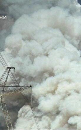 Massive white smoke plume behind a high-voltage transmission tower and lines; emergency services logo in the top-left corner.