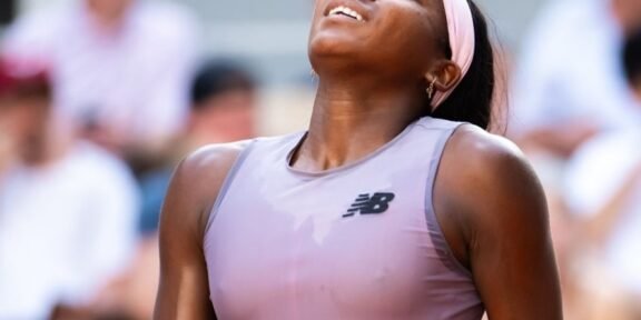 Athlete in a lavender sleeveless top and pink headband looks up with a smile as a crowd blurs in the background.