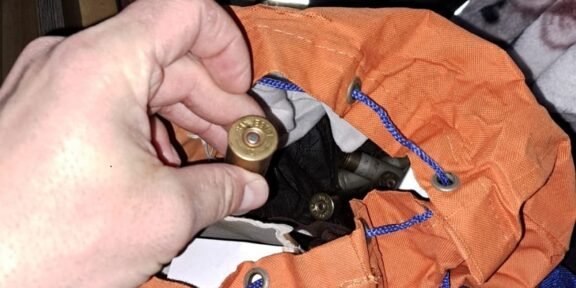 Close-up of a hand holding a brass shotgun shell over an orange bag with blue cords; inside are more shells, Romanian police logo visible