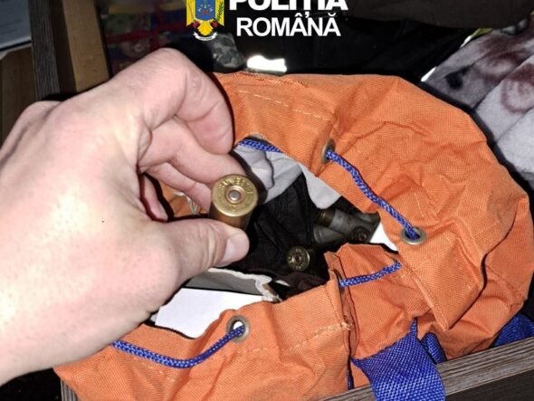 Close-up of a hand holding a brass shotgun shell over an orange bag with blue cords; inside are more shells, Romanian police logo visible