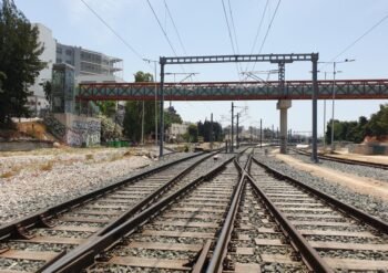 Railway tracks split and converge under overhead wires to the horizon, with graffiti walls on the left and a red bridge above.
