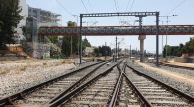 Railway tracks split and converge under overhead wires to the horizon, with graffiti walls on the left and a red bridge above.