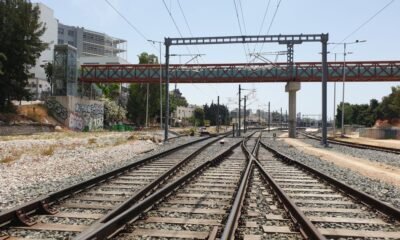Railway tracks split and converge under overhead wires to the horizon, with graffiti walls on the left and a red bridge above.