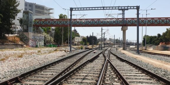 Railway tracks split and converge under overhead wires to the horizon, with graffiti walls on the left and a red bridge above.