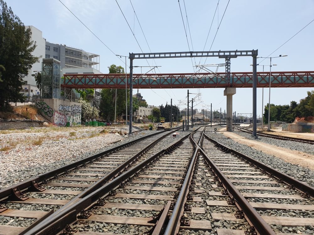 Railway tracks split and converge under overhead wires to the horizon, with graffiti walls on the left and a red bridge above.