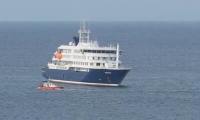 Large white and blue luxury yacht on calm open water with a small red dinghy nearby.