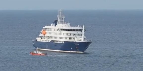 Large white and blue luxury yacht on calm open water with a small red dinghy nearby.